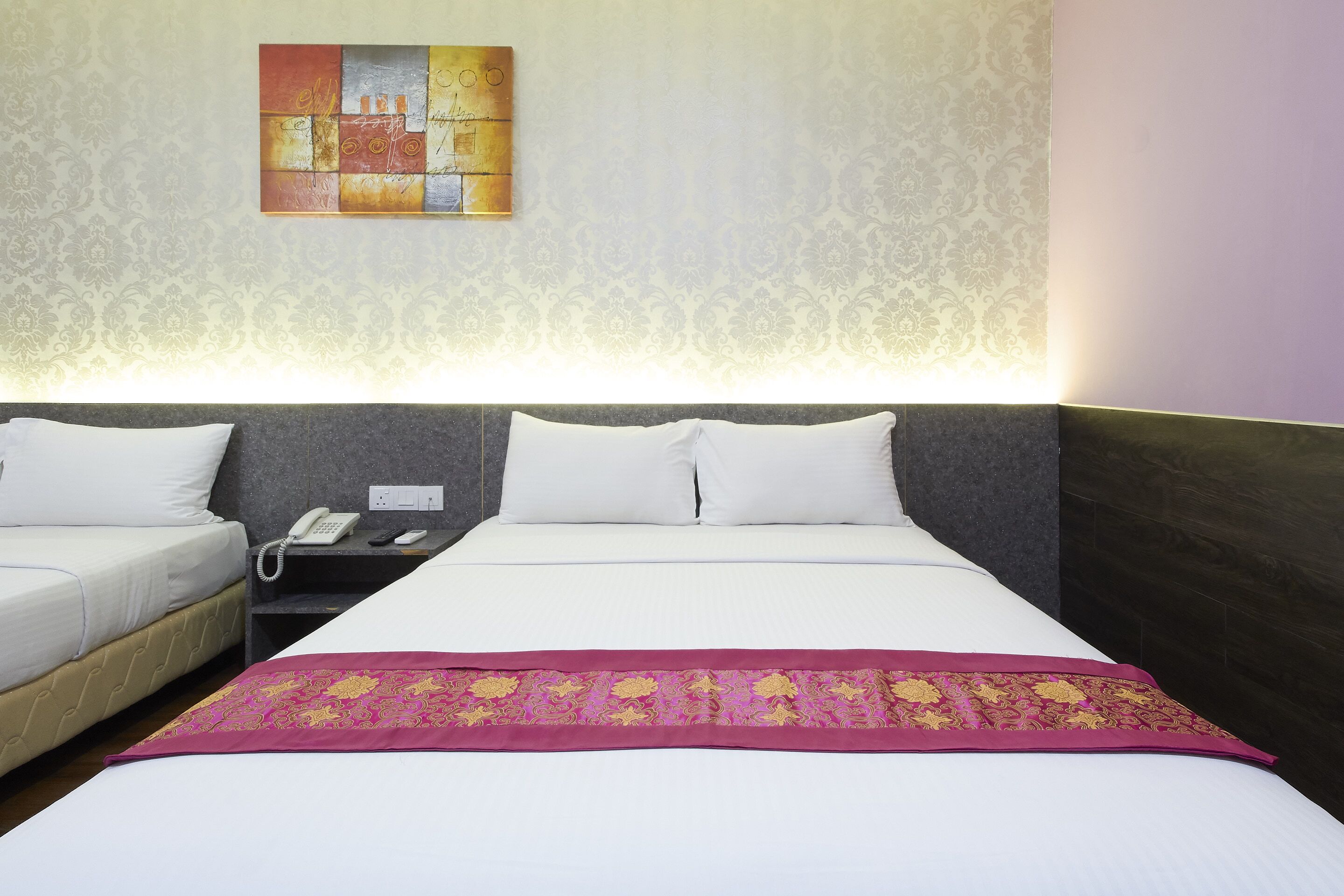 A hotel room with two beds, a nightstand with a phone, and a decorative wall piece.