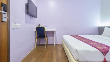 Una habitación con cama, escritorio, silla, televisor y toma de corriente en la pared.