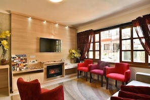 A modern living room with a flat-screen TV, a fireplace, and red chairs. - Pousada Stillo Gramado (Gramado)