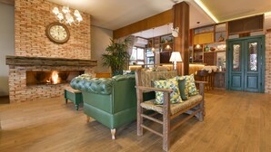 A cozy living room with a brick fireplace, green sofas, and a wooden chair. - Hotel Bertoluci (Gramado)