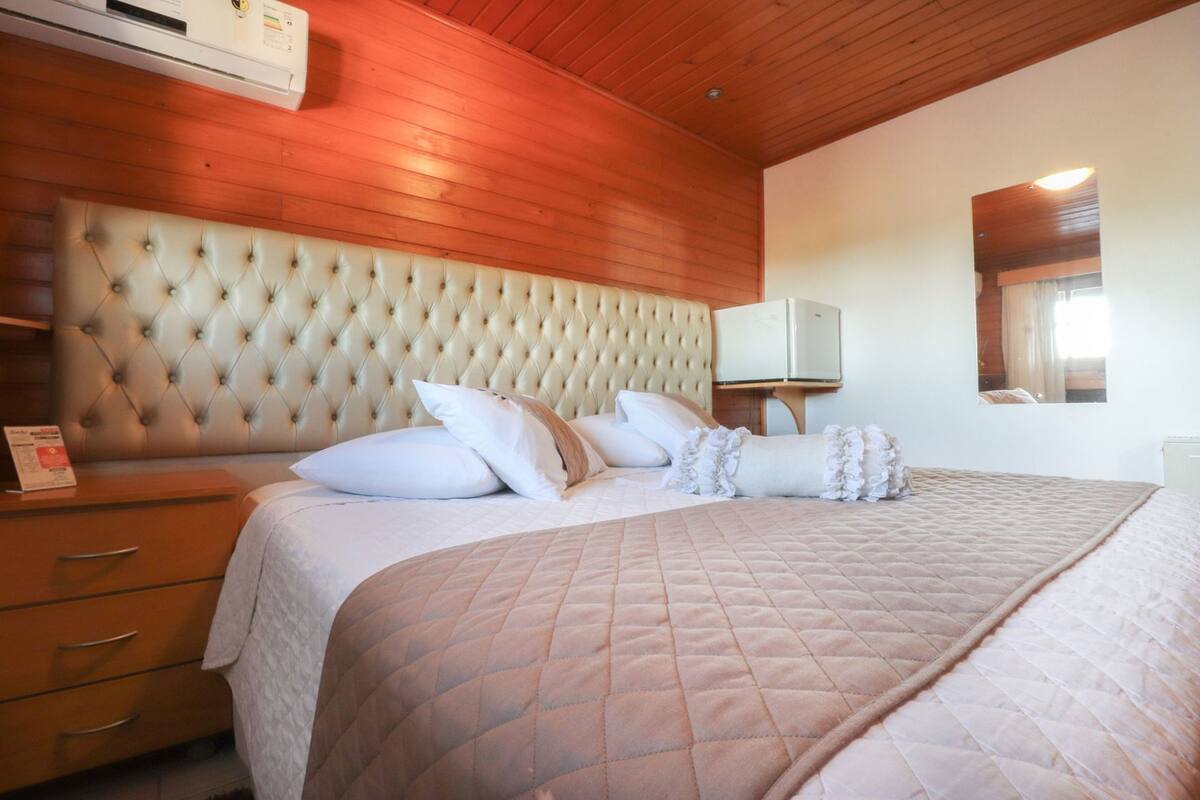 A bedroom with a tufted headboard, a bed with a quilted cover, a bedside table, and a mirror on the wall.