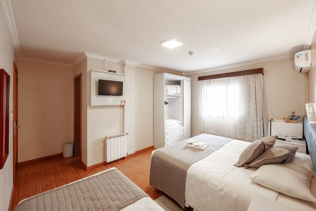 A hotel room with two beds, a TV, a wardrobe, a radiator, and a window with curtains.