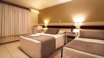 Una habitación de hotel con dos camas individuales, una mesita de noche, una lámpara y un ventanal con cortinas.
