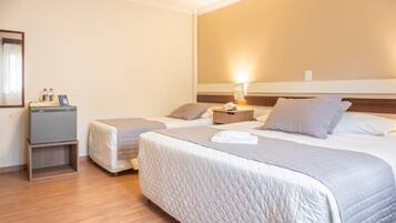 A hotel room with two beds, a bedside table with a lamp, a small desk with a chair, and a mirror on the wall.
