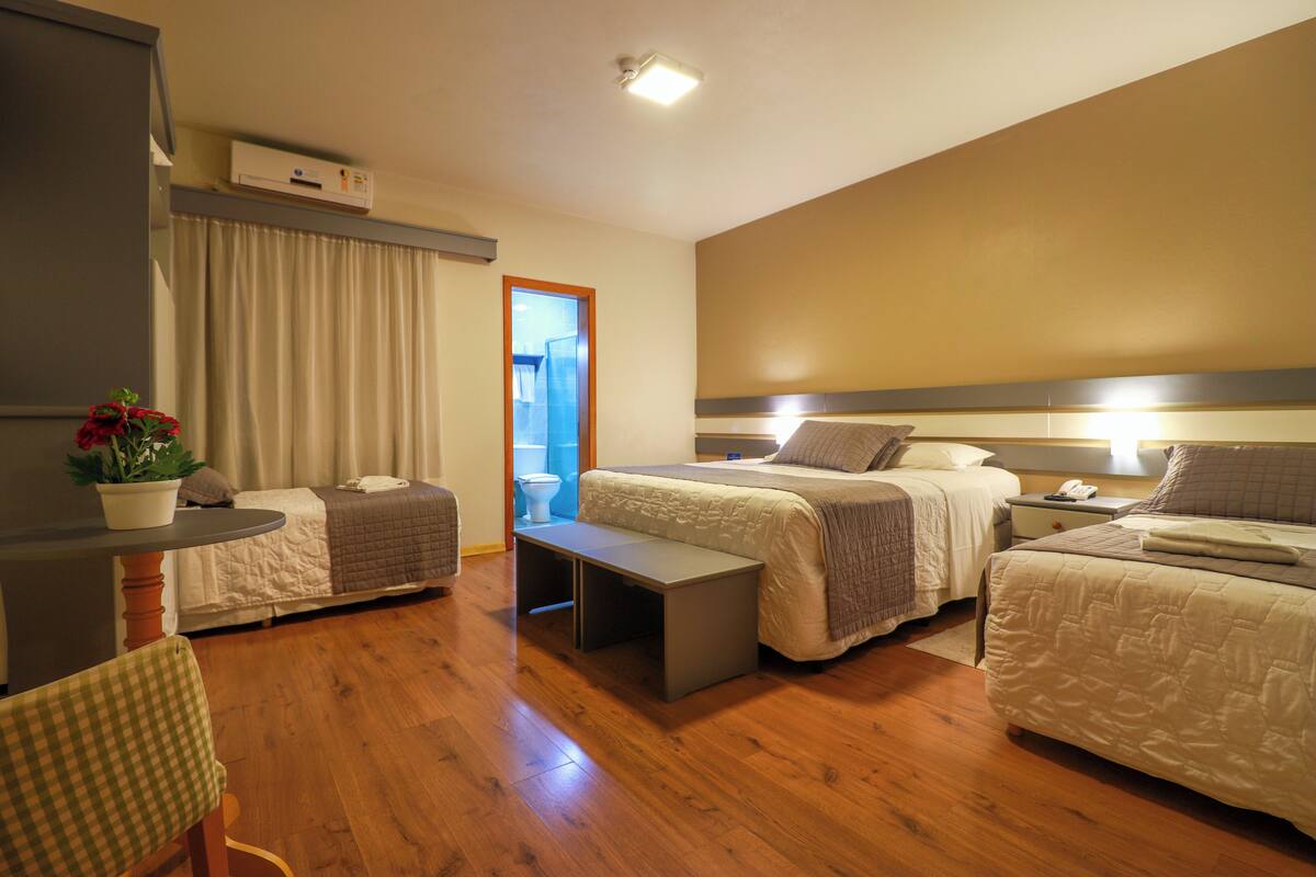 A hotel room with two beds, a small table, a bench, a chair, and a potted plant.