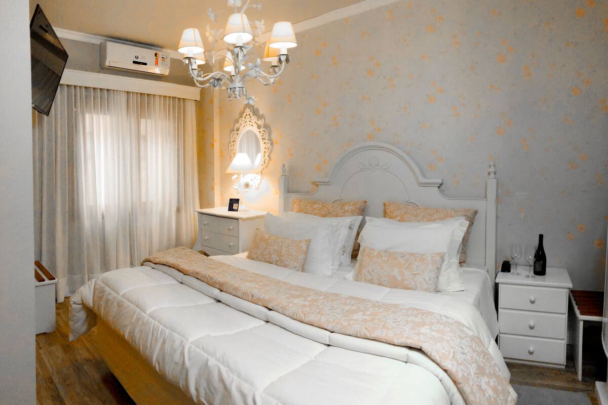 A neatly arranged bedroom with a large bed, bedside tables, a mirror, and a chandelier.
