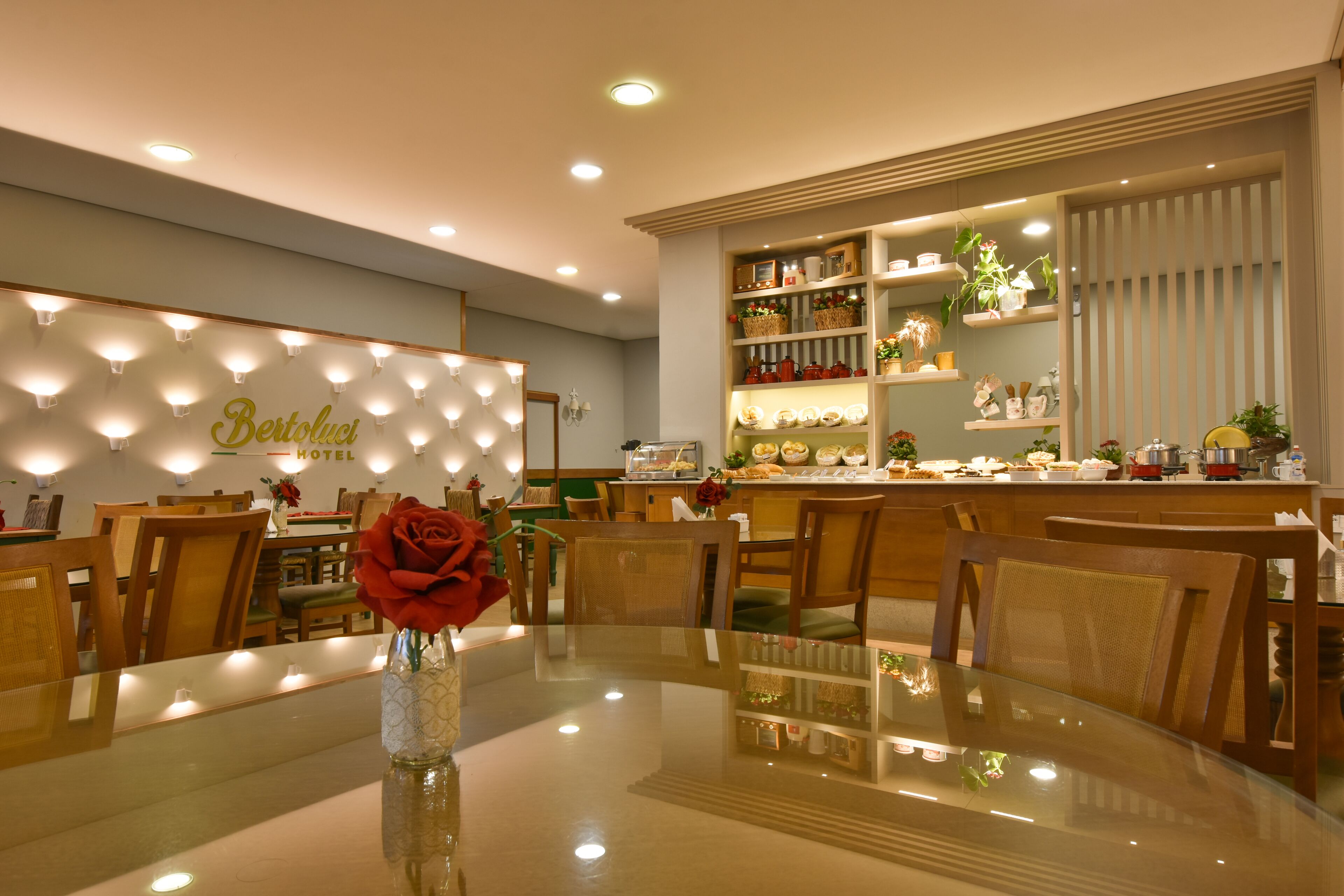 Eine Hotelhalle mit einem runden Glastisch, Holzstühlen, einer Vase mit einer roten Rose und einer Wand mit beleuchteten Lichtern sowie einem Schild mit der Aufschrift 'Bistoli Hotel'.