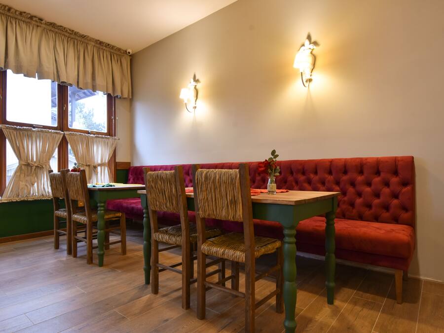 Un comedor con un sofá tapizado rojo, sillas de madera, una mesa de madera y dos lámparas fijadas a la pared.