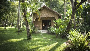 A thatched-roof hut surrounded by lush greenery and a stone pathway leading to it. - Maison Polanka (Siem Reap)