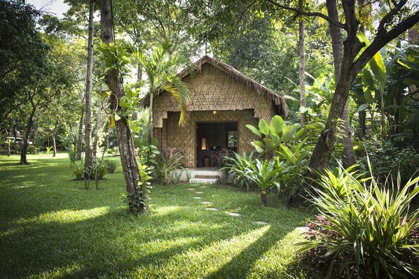 A thatched-roof hut surrounded by lush greenery and a stone pathway leading to it. - Maison Polanka (Siem Reap)