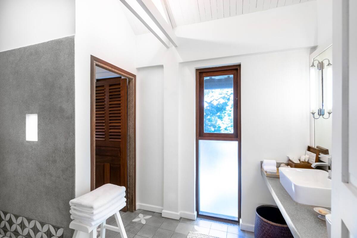 A bathroom with a large window, a white sink, and a wooden door.