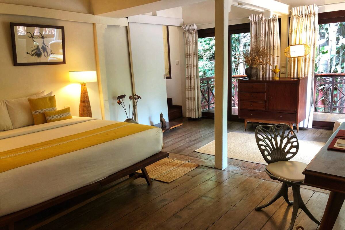 A hotel room with a bed, a desk, a chair, a lamp, and a view of the outdoors.