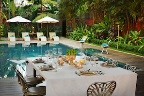A poolside dining area with a table set for a meal, surrounded by lounge chairs and umbrellas. - Maison Polanka (Siem Reap)