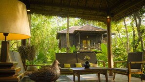 A wooden deck with a sofa, chairs, a table, and a lamp. There is a bird sculpture on the table and a view of a building in the background. - Maison Polanka (Siem Reap)