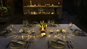 A table set for a meal with a candle centerpiece, surrounded by chairs and dining utensils. - Maison Polanka (Siem Reap)