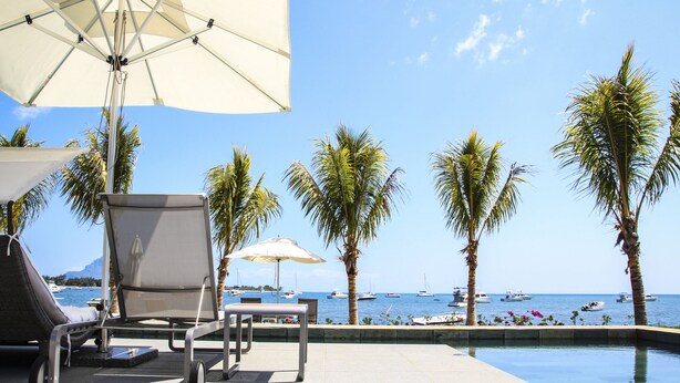 Zona de piscina con sillones de descanso, sombrillas y vista al mar con barcos.