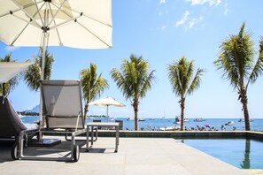 A poolside area with lounge chairs, umbrellas, and a view of the sea with boats. - Latitude Luxury Seafront Apartments (Black River)