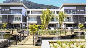 Un hotel moderno con zona de piscina, mobiliario exterior y montañas al fondo.