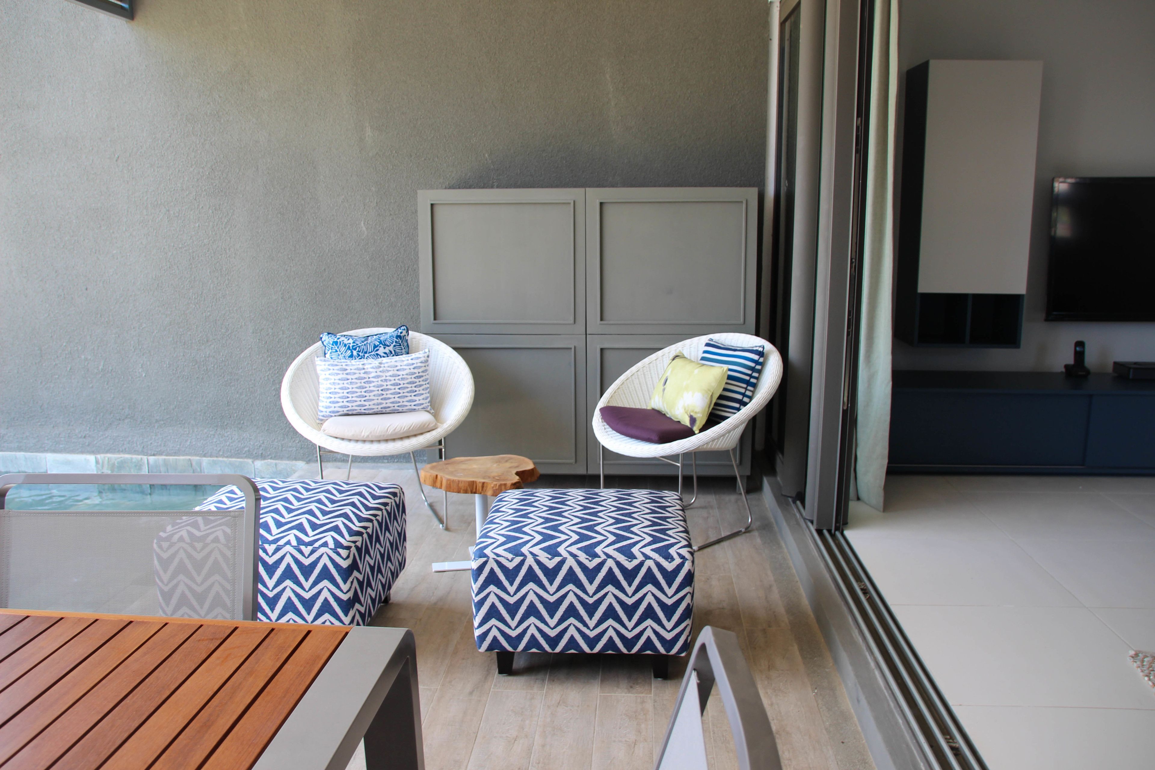 Un espace extérieur moderne aménagé avec deux chaises et un banc, une table en bois, et une vue sur une piscine et un espace cuisine.