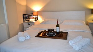 A neatly made bed with a tray of wine glasses, a bottle, and a bowl of blueberries. - Hotel GNG (Tbilisi)