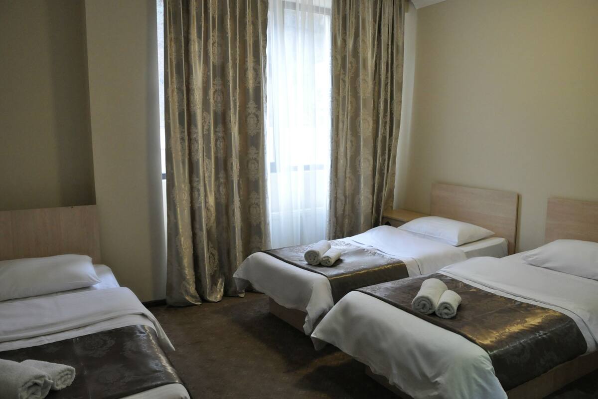 Habitación de hotel con dos camas, una ventana con cortinas y un cabecero de madera.