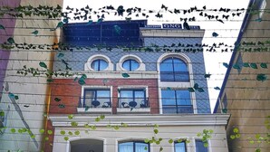 A two-story building with a large arched window at the ground level, a balcony with a metal railing, and a sign for "GNC Hotel" above the entrance. - Hotel GNG (Tbilisi)
