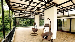 A covered balcony with wicker chairs, wooden flooring, and a view of greenery. - Hotel GNG (Tbilisi)
