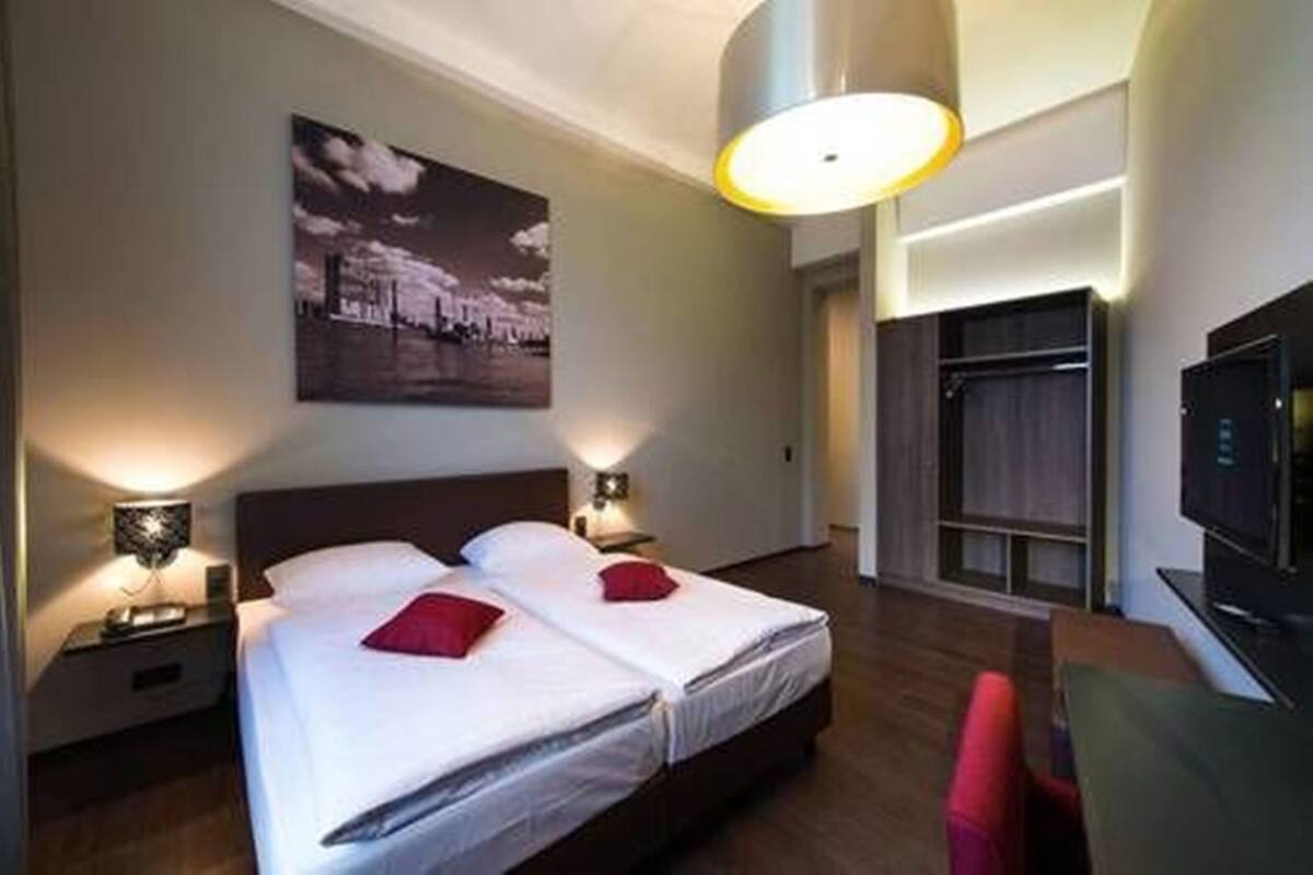 Habitación de hotel con dos camas, un escritorio, un televisor y un ventanal amplio.