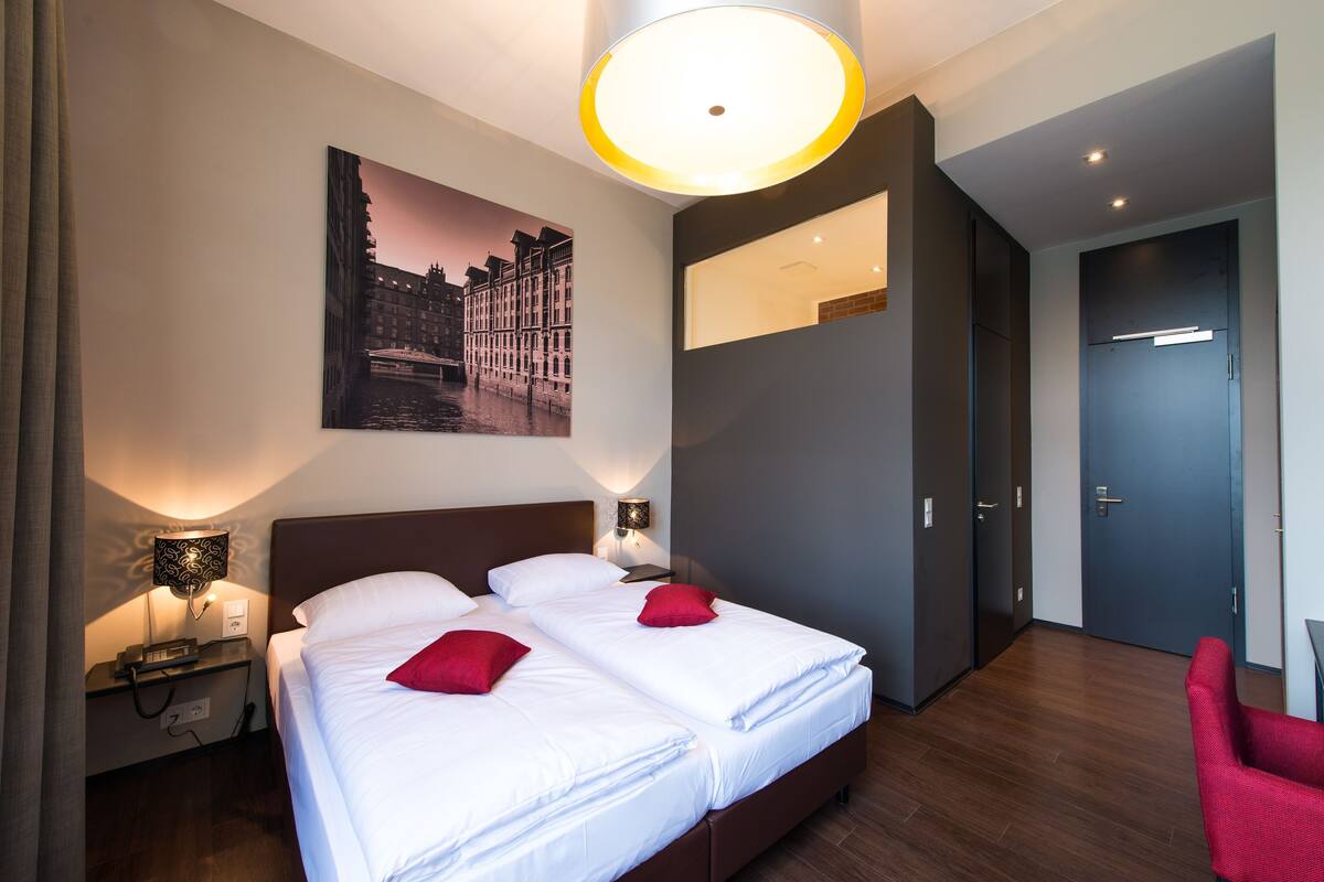 Una habitación de hotel con dos camas, un escritorio, una silla, un cuadro y una puerta.
