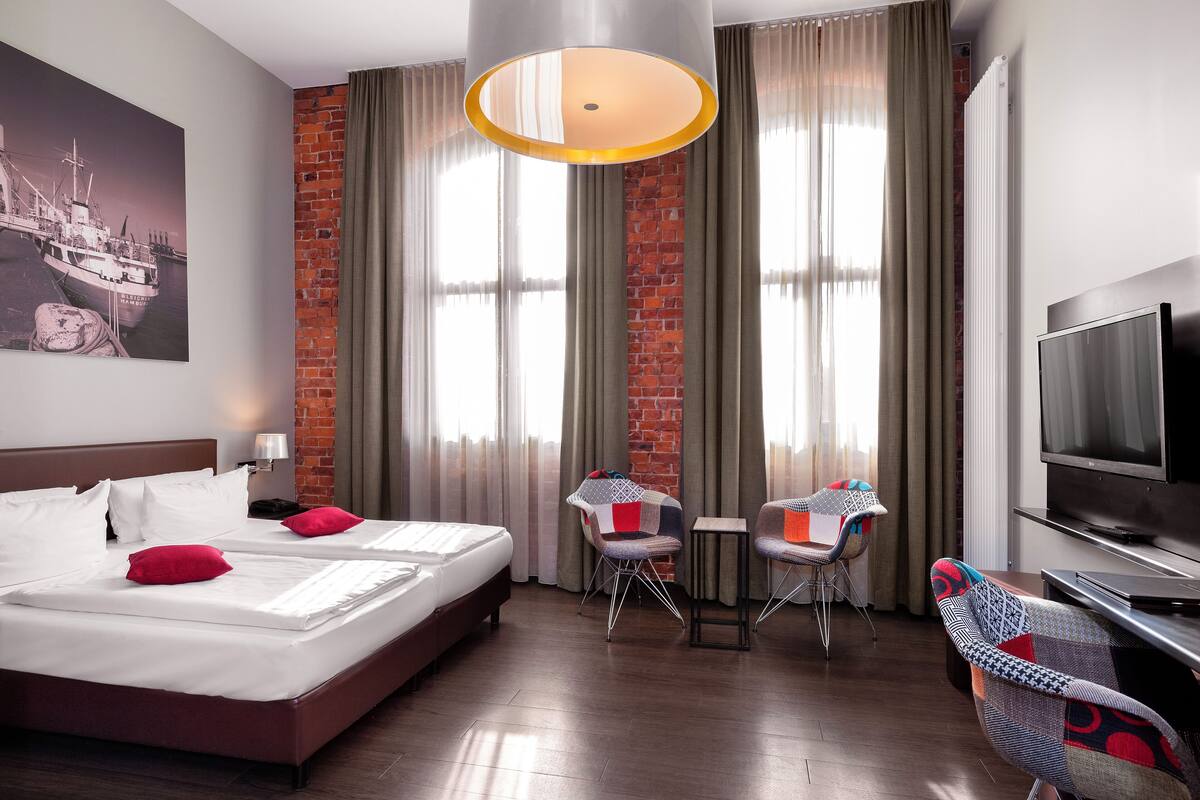 Una habitación de hotel con una cama grande, dos sillas, una mesita pequeña, un televisor y una pared de ladrillo.