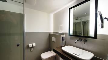 A modern bathroom with a glass shower enclosure, a white toilet, a sink with a large mirror, and a towel rack.