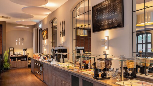 A buffet area with various food stations, a coffee machine, and a menu board on the wall. - Hotel Volksschule (Hamburg)