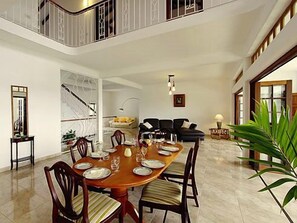 A spacious dining area with a high ceiling, a staircase, and a living area with a sofa and a lamp. - La Residence (Mahé Island)