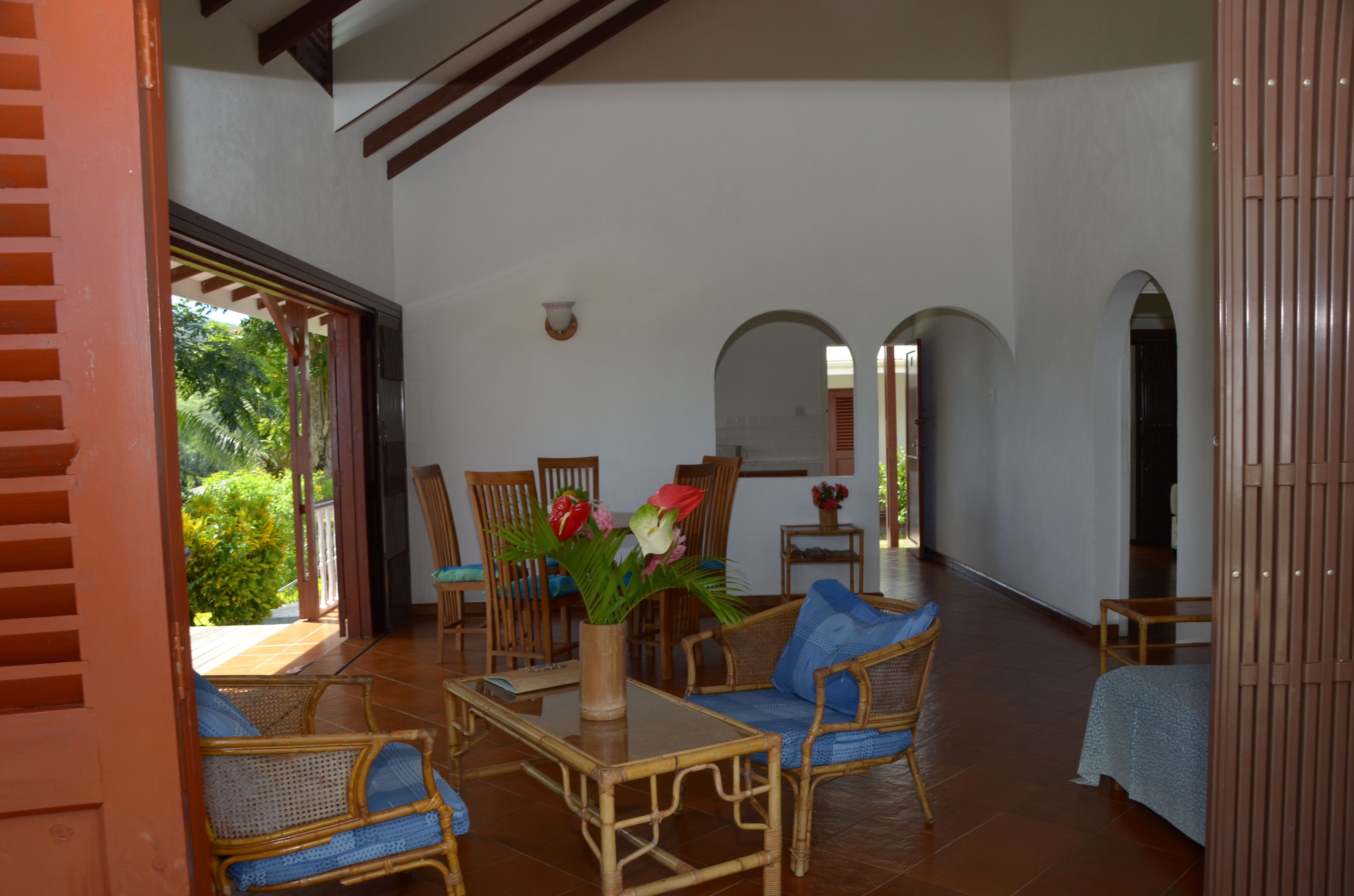 A spacious room with a large open area, a dining table with chairs, a sofa, and a small table with a vase of flowers.