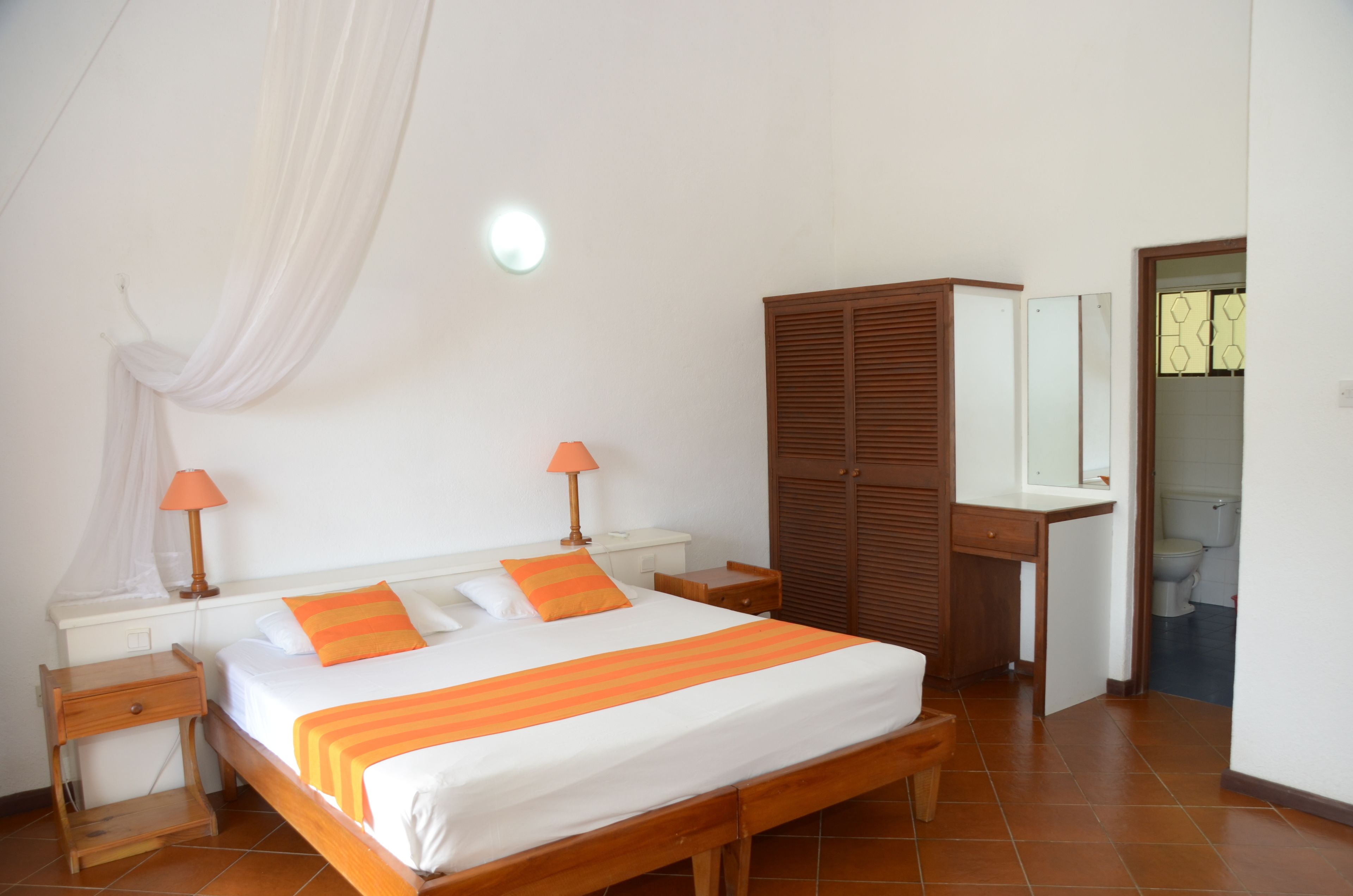 Une chambre à coucher avec un lit, des tables de chevet, une armoire et une salle de bain visible à travers une porte ouverte.