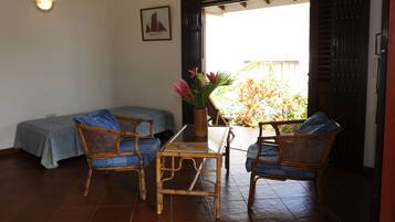 Una habitació amb un llit, dues cadires de vimetla, una taula petita i un ram de flors.