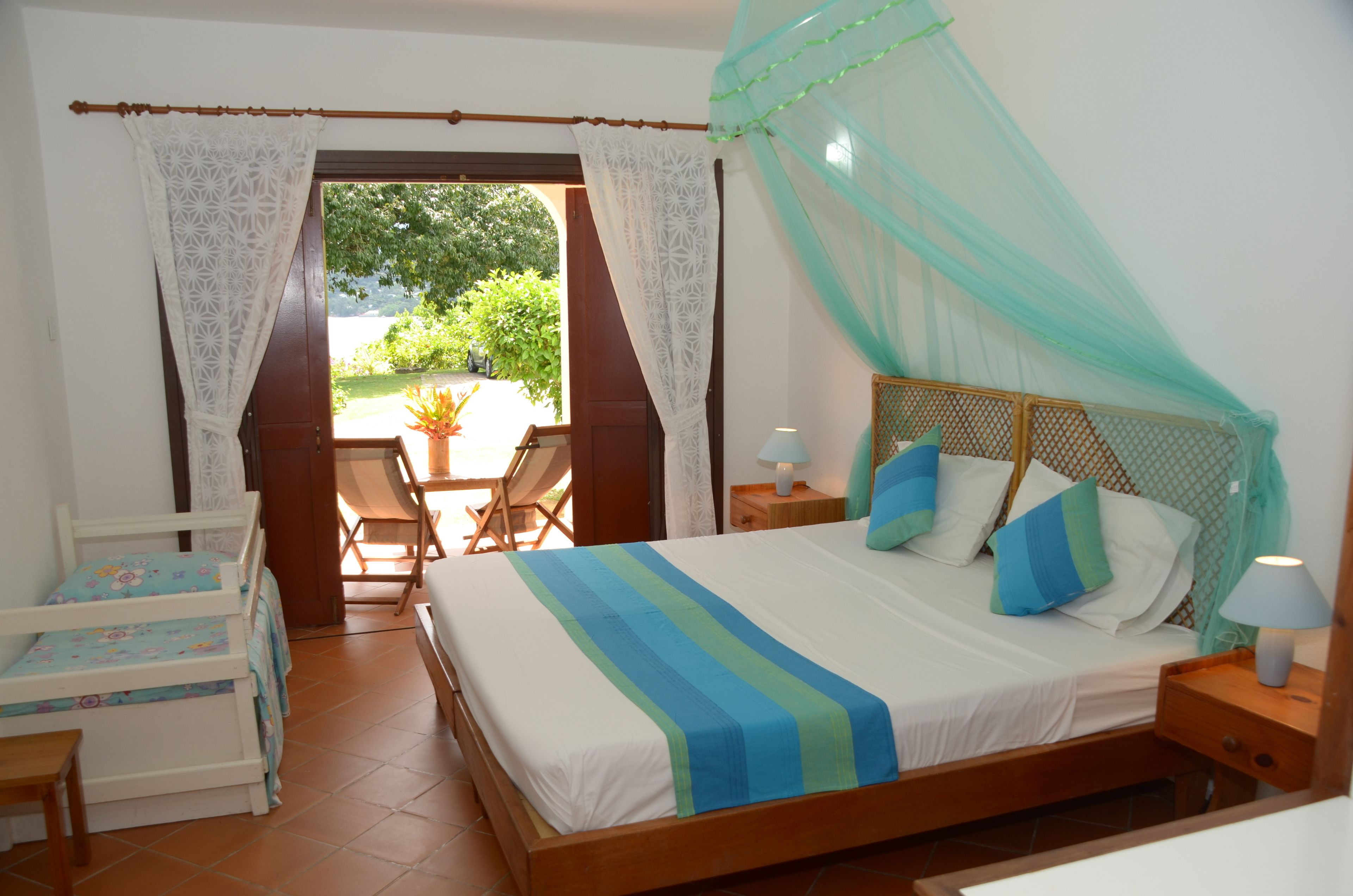 Un dormitorio con cama, mesita de noche, silla y ventana con cortinas.