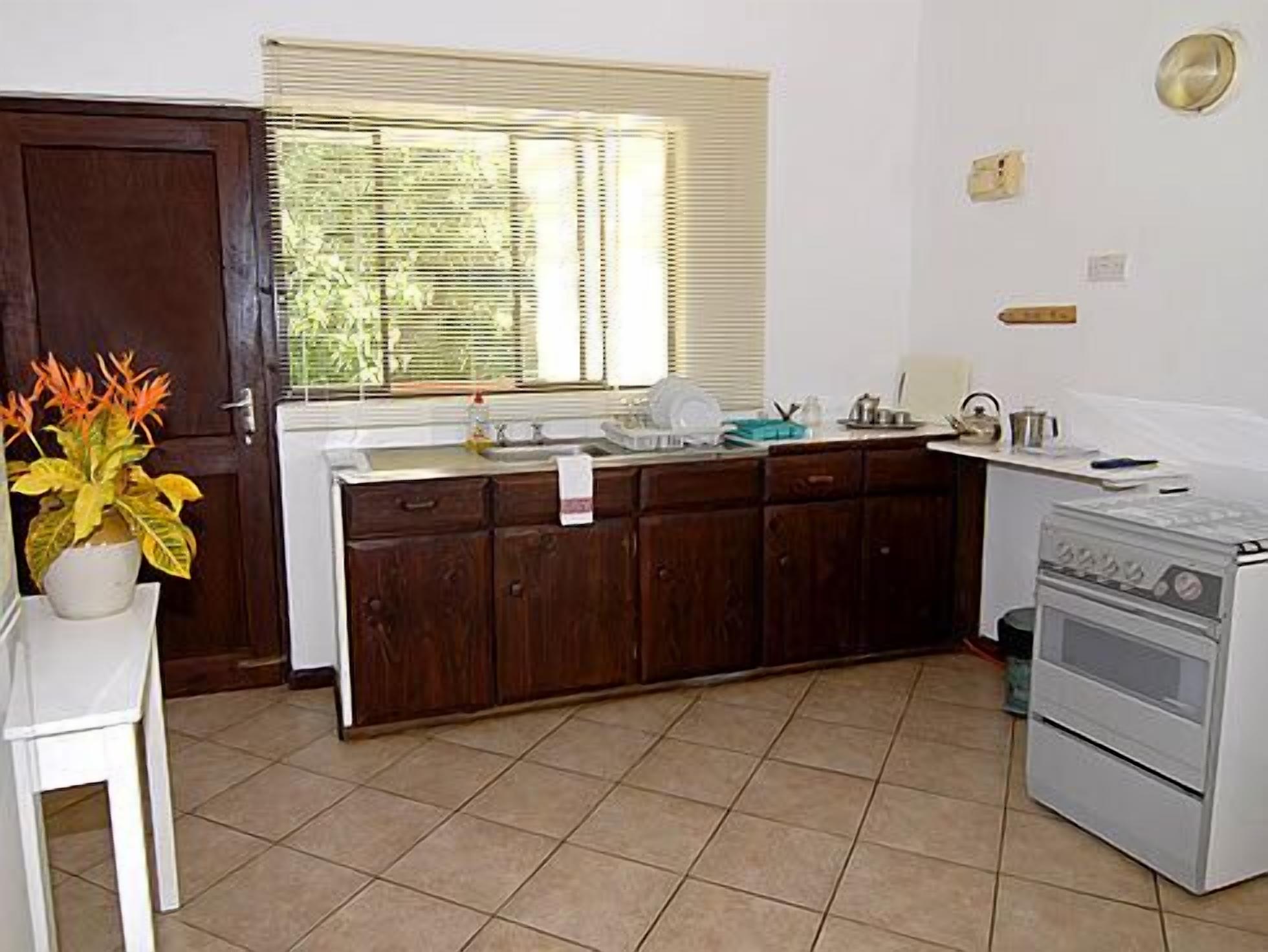 Une cuisine avec des meubles de rangement en bois, une cuisinière, un évier et une fenêtre équipée de stores.