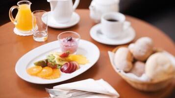 Une table mise pour le petit-déjeuner avec une assiette de fruits, un pichet de jus d’orange, une tasse de café et un bol de viennoiseries.