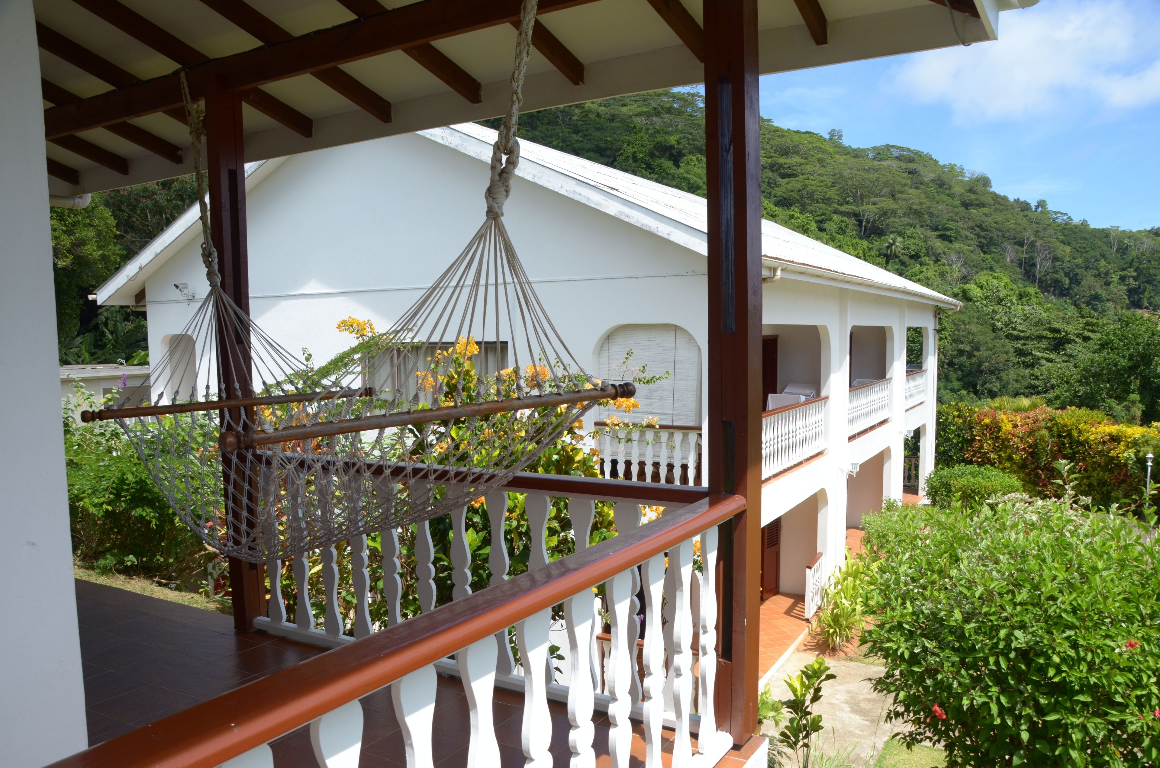 A white building with a balcony, surrounded by lush greenery and hills.