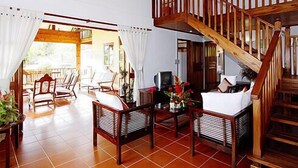 A spacious room with a wooden staircase, wicker furniture, and a view of the outdoors. - La Residence (Mahé Island)