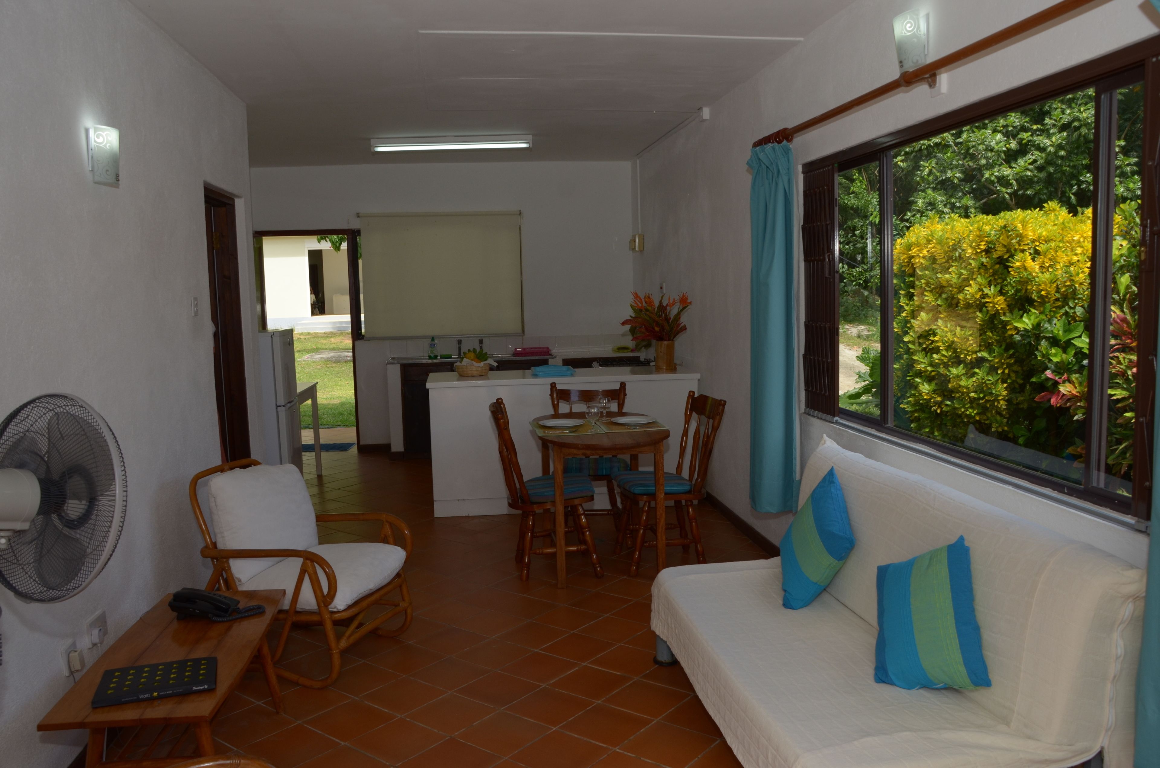 Un espacio habitable compacto con comedor, un sofá con cojines, un ventilador y una ventana con vistas a zonas verdes.