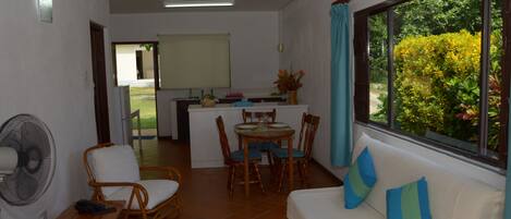 Un espacio habitable compacto con comedor, un sofá con cojines, un ventilador y una ventana con vistas a zonas verdes.