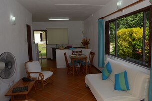 Un espacio habitable compacto con comedor, un sofá con cojines, un ventilador y una ventana con vistas a zonas verdes.
