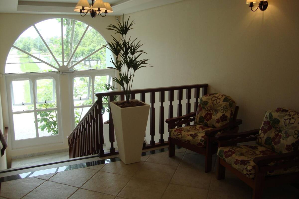 Une pièce spacieuse avec une grande fenêtre en arc de cercle, une plante en pot, une chaise en bois et un escalier muni d’une rampe.