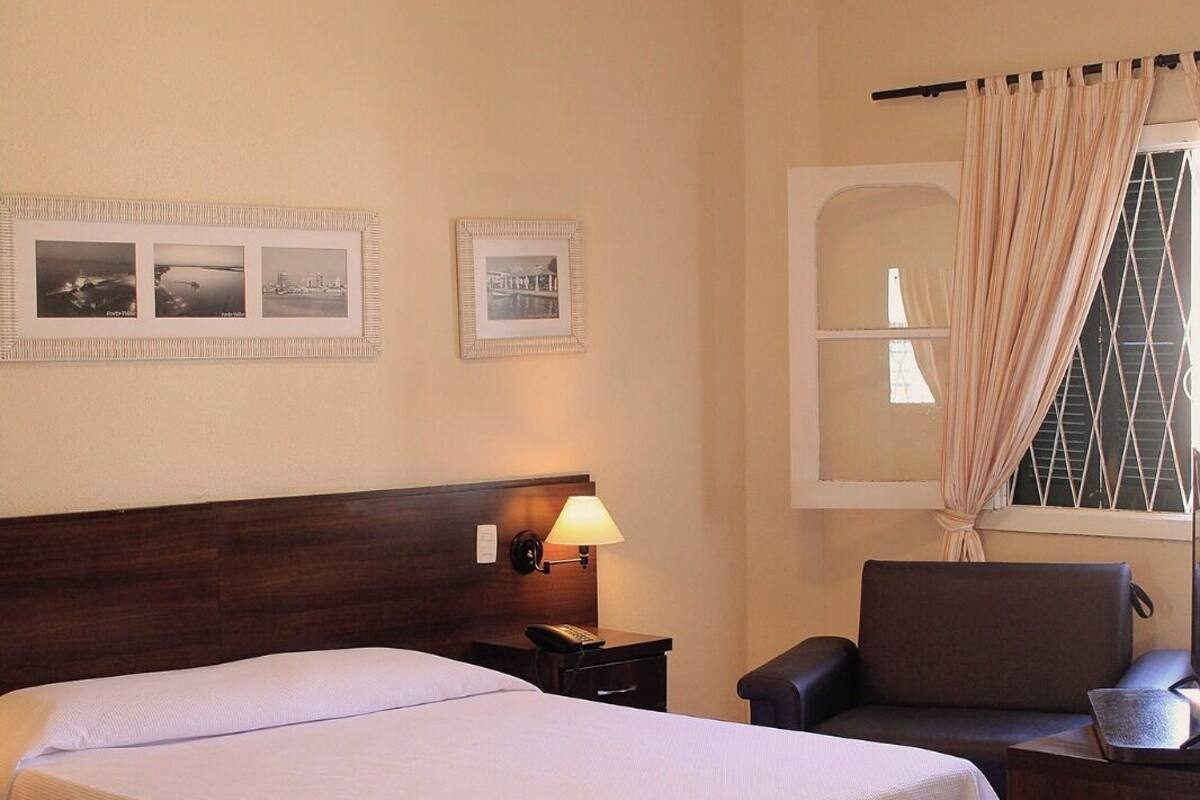 Une chambre d’hôtel avec un grand lit, un bureau avec une lampe, une chaise et une fenêtre avec des rideaux.