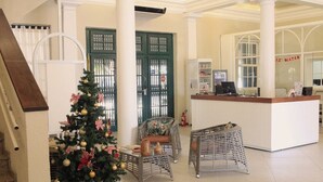 Un hall d’entrée décoré d’un sapin de Noël, avec des fauteuils en osier, un comptoir d’accueil et un escalier.