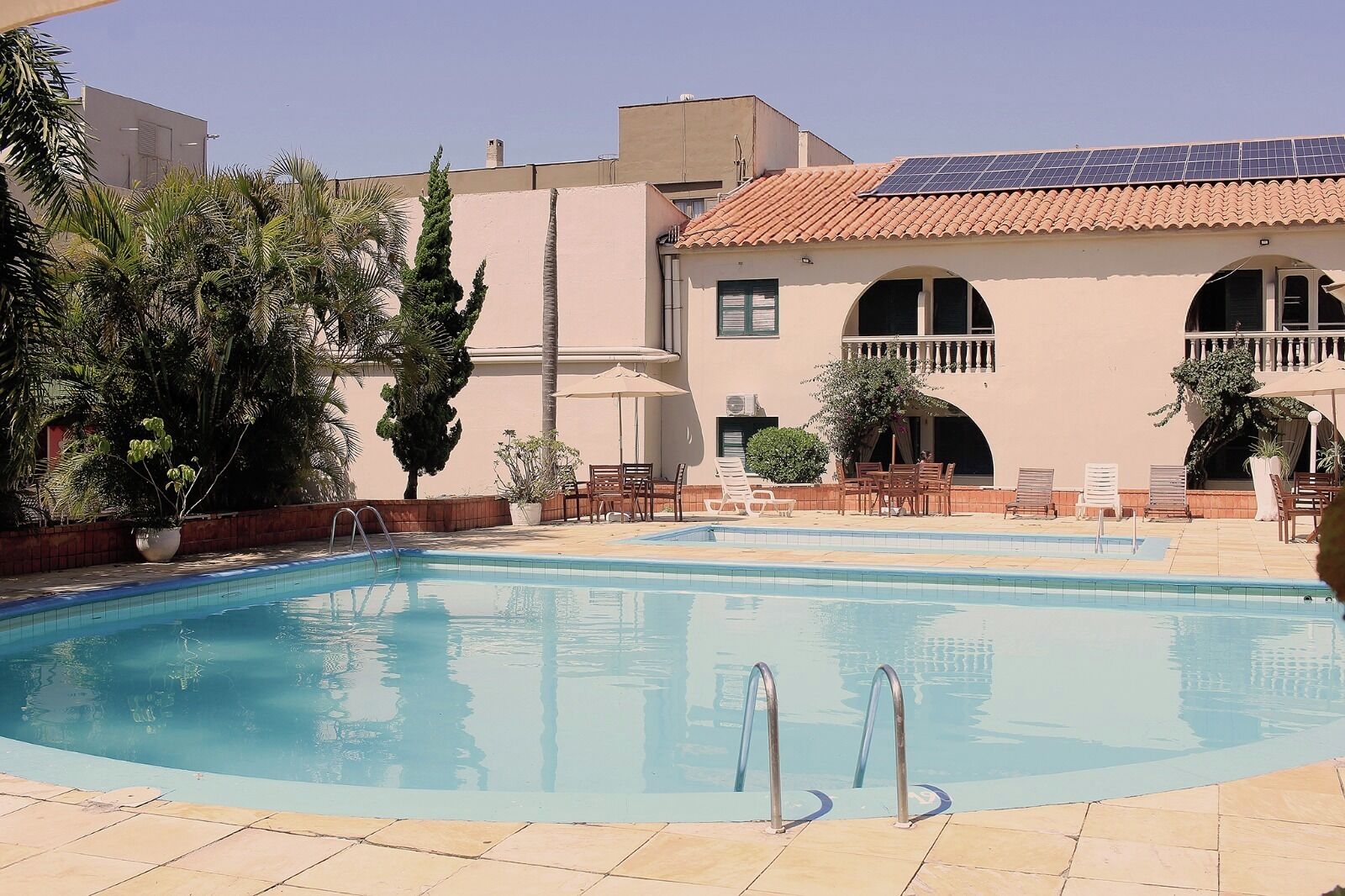 Una piscina con sillones de descanso y un edificio con tejado de baldosas y ventanas arqueadas.