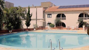 Una piscina con sillones de descanso y un edificio con tejado de baldosas y ventanas arqueadas.
