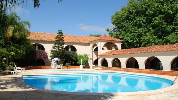 Une piscine dotée d’une terrasse carrelée, entourée d’un bâtiment aux fenêtres en arc de cercle et au toit recouvert de tuiles.